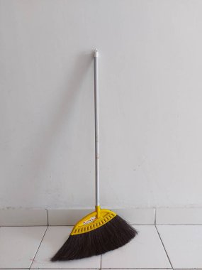 Bogor, Endonezya-11 Mart 2022: Beyaz fayanslı zeminde beyaz bir duvara yaslanmış bir süpürge. Metin ya da alıntı için çok yer