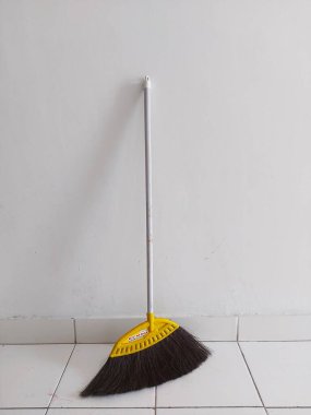 Bogor, Endonezya-11 Mart 2022: Beyaz fayanslı zeminde beyaz bir duvara yaslanmış bir süpürge. Metin ya da alıntı için çok yer
