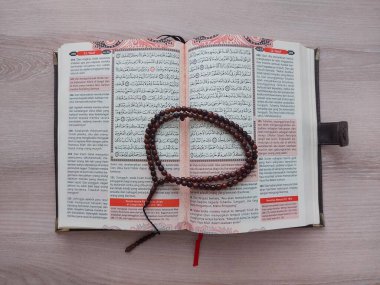 Bogor, Endonezya-4 Mart 2022: Müslümanların kutsal kitabı ya da tahta masanın üzerindeki Kur 'an. Kahverengi ahşap dua boncuklarıyla donatılmış. izole edilmiş. Boşluğu kopyala