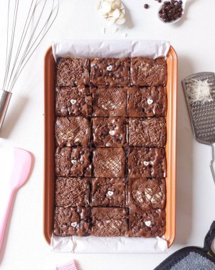 Fırında pişmiş çikolatalı kek. Peynir soslu, çikolata parçacıklı badem ve çikolata ezmeli. Fırça, peynir rendesi, fırça, spatula ve beyaz kaşıkla tamamlanmış. İzole edilmiş arkaplan beyaz.