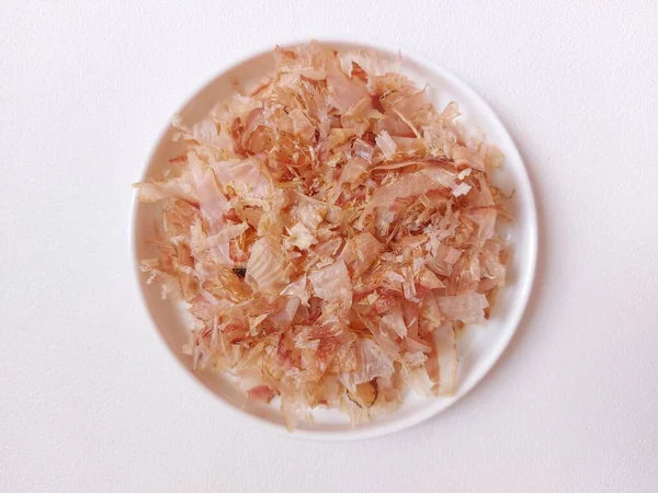Katsuobushi. It is preserved food made from skipjack tuna. shaved like wood shavings for the broth. basis of Japanese cuisine, sprinkled on top of food as a flavoring. eaten as a side dish with rice