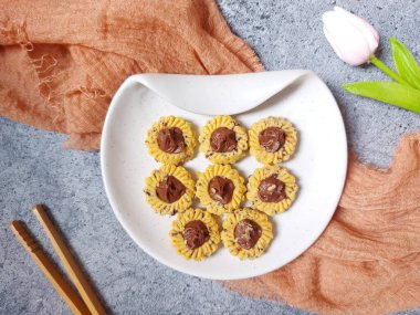 Çikolatalı tart kurabiyeleri. Beyaz tabakta servis ediliyor. un, yumurta sarısı, margarin, mısır nişastası, tereyağı, süt, arıtılmış şeker, tuz, çikolata parçacıkları ve vanilya özünden yapılır. Çikolata ezmesiyle süslenmiş.