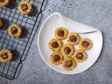 Çikolatalı tart kurabiyeleri. Beyaz tabakta servis ediliyor. un, yumurta sarısı, margarin, mısır nişastası, tereyağı, süt, arıtılmış şeker, tuz, çikolata parçacıkları ve vanilya özünden yapılır. Çikolata ezmesiyle süslenmiş.