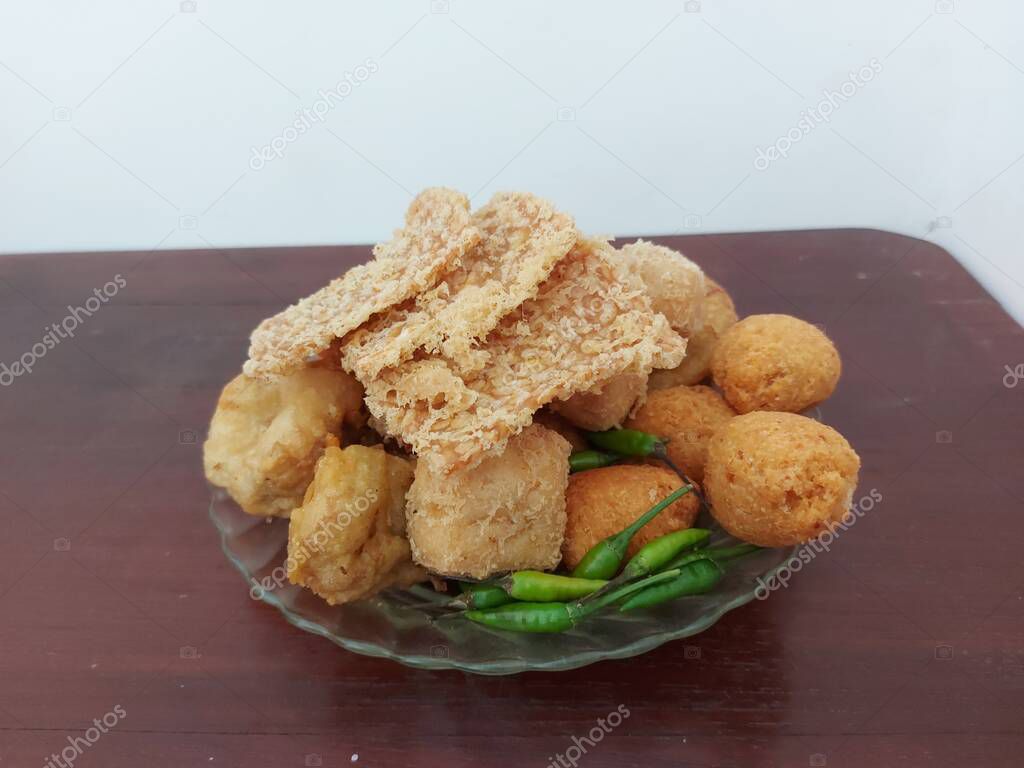 assorted fried snacks.  Indonesian snacks.  consisting of fried tempeh, combro, fried tofu and bakwan.  with raw green chilies.  delicious and savory. served on plate.