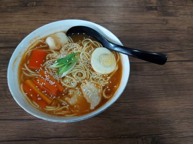 Beyaz kasede ramen eriştesi. Japonya 'dan geleneksel yemek. Lezzetli bir tat. Haşlanmış yumurta, tavuk, susam tohumu, havuç, taze soğan, yengeç çubuğu, chikuwa. Tahta masada servis edilir.. 