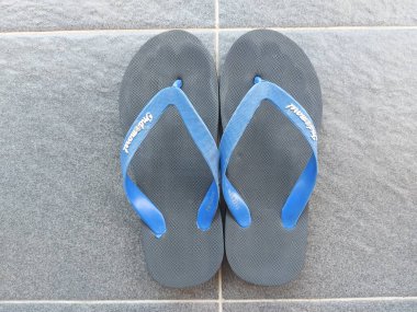 Bandung,Indonesia-July 8 2022: black rubber sandal with blue strap on grey floor. indomaret brand. 