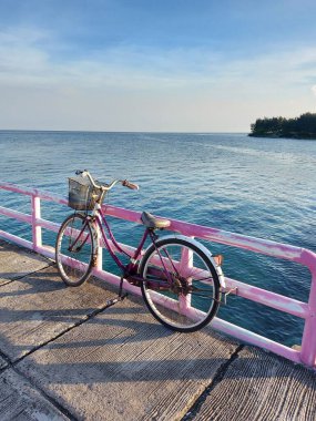 Jakarta, Endonezya-23 Temmuz 2022: iskeleye yaslanmış pembe bisiklet. Deniz manzaralı ve mavi gökyüzü