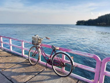 jakarta,indonesia-july 23 2022: pink bicycle leaning against the pier railing.  with a view of the sea and blue sky
