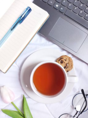 bogor, indonesia-august 5 2022: Break time concept. A cup of tea. Completed with laptop, blank book,blue pen, glasses, tulip flower and white plate.