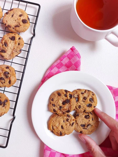 Chocolate chips cookies on white plate and the cooling rack. Sweet and delicious taste. Soft but crunchy. Completed with tea on a cup. Top view. Flat lay. Minimalist and aesthetic food photography.