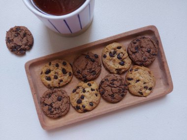 Tea time photography concept.  A cup of tea with choco chips cookies on wooden plate. Isolated background in white. Minimalist and aesthetic photo.