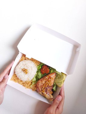 Beyaz karton kutuda Hainanese tavuğu pilavı. Kızarmış un, çiğ sebze ve kırmızı acı biber sosuyla birlikte. Singapur 'da popüler bir yemektir. Lezzetli. Yemek ayarla. İzole edilmiş arkaplan beyaz