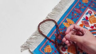 Kadın eli, mavi bir halıdaki ahşap dua boncuklarıyla anma yapıyor.