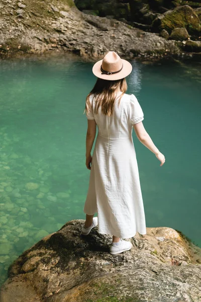 一个身穿白色长裙、头戴白色帽子的漂亮女人站在水边笑着。旅行概念. — 图库照片
