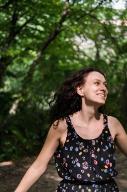 Kıvırcık saçlı güzel bir kadın, yüzünün yarısı ağacın arkasında saklı. Doğayla birlik.