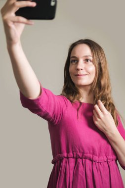 Pembe elbiseli, uzun saçlı genç bir kadın evde selfie çekiyor..