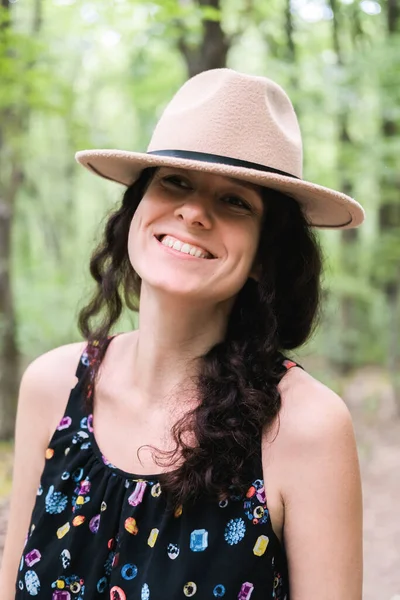 Joven mujer milenaria en vestido y sombrero beige se encuentra en el bosque feliz y relajado, disfruta de la naturaleza y la tranquilidad. Concepto de viaje solo. Imágenes de stock libres de derechos