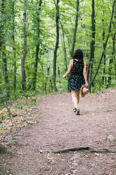 Joven mujer milenaria en vestido y sombrero beige se encuentra en el bosque feliz y relajado, disfruta de la naturaleza y la tranquilidad. Concepto de viaje solo. Fotos de stock libres de derechos