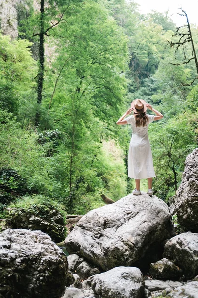 Joven mujer milenaria en vestido y sombrero beige se encuentra en el bosque feliz y relajado, disfruta de la naturaleza y la tranquilidad. Concepto de viaje solo. Imágenes de stock libres de derechos