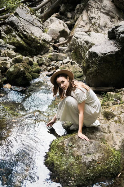 Hermosa mujer en vestido largo blanco y sombrero está sentado junto al río y sonriendo. Concepto de viaje. Imagen De Stock