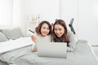 Evde kredi kartı ve laptopla online alışveriş yapan iki mutlu kadın. 