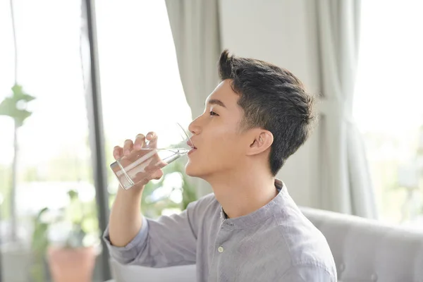 Gelukkig Aziatische Guy Zitten Bank Drinken Water Thuis — Stockfoto