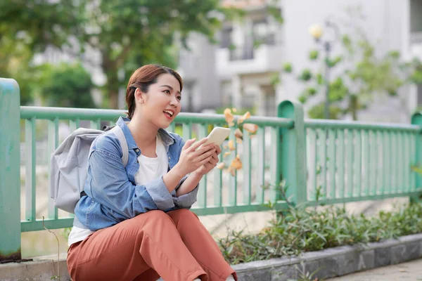 美しい若いアジアの女性の肖像画笑顔ながら 携帯電話を保持外に座って — ストック写真