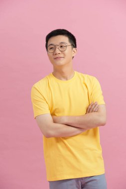 Genç adam pembe arka planda kollarını kavuşturuyor.