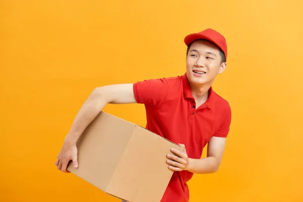 开朗的送货人 快乐的年轻信使拿着一个纸板盒和微笑 而站立反对白色背景 — 图库照片