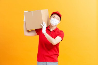 Koruyucu maskeli bir kurye ve elinde karton kutu tutan tıbbi eldivenler.