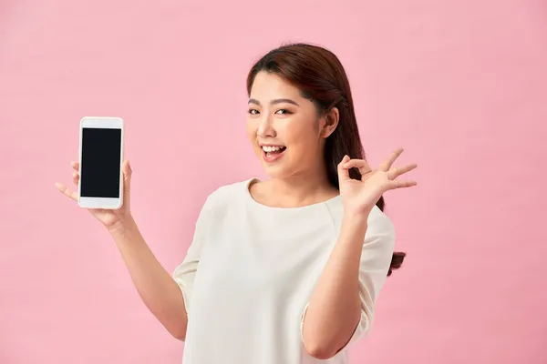 快乐的亚洲肖像画漂亮可爱的年轻女子兴奋地拿着手机 摆出一副不错的手势 工作室用粉色背景拍摄 — 图库照片