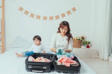 Sevimli bebek, annesinin yanına oturur. Giysileri valize koymak için hazırlar.