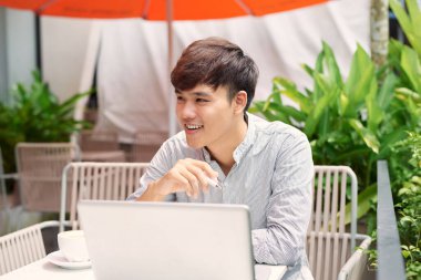 Ücretsiz wi-fi avantajları kullanarak. dizüstü bilgisayarda çalışan ve kaldırımda kafede otururken gülümseyen yakışıklı delikanlı