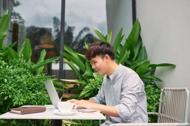 Genç adam dışarıda çalışmak için dizüstü bilgisayar kullanıyor.