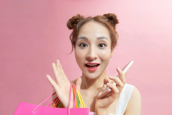一个年轻的亚洲女人的肖像 带着五颜六色的购物袋 享受着与粉色背景隔离的移动技术 — 图库照片