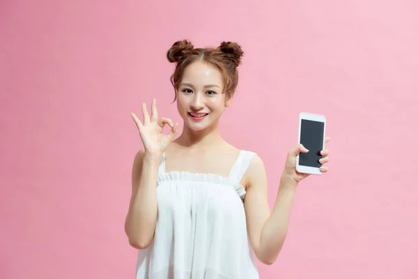 魅力的な若いです女の子ショーOkジェスチャーともに角質スクリーン携帯電話絶縁上のピンクの背景 — ストック写真