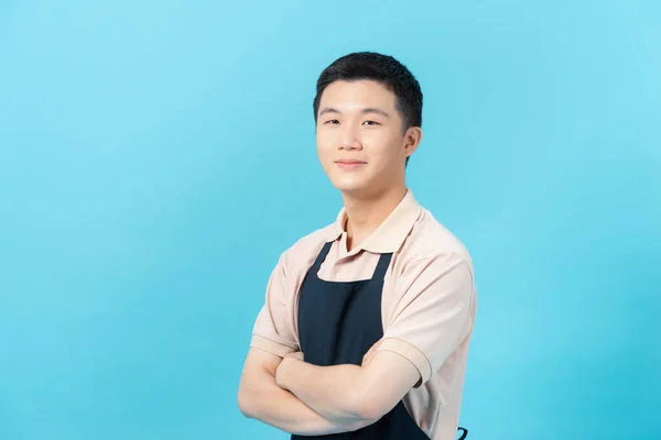 Handsome guy arms crossed friendly smiling positive good mood professional worker wear apron isolated on light blue background