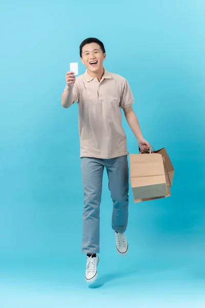 快乐地笑着 英俊的亚洲男人提着购物袋 拿着浅蓝色的信用卡 — 图库照片