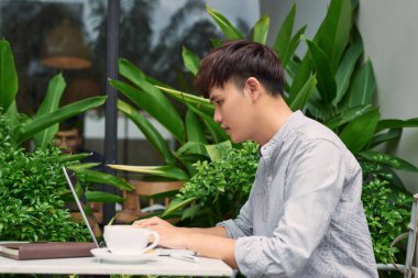 Ücretsiz wi-fi avantajları kullanarak. dizüstü bilgisayarda çalışan ve kaldırımda kafede otururken gülümseyen yakışıklı delikanlı