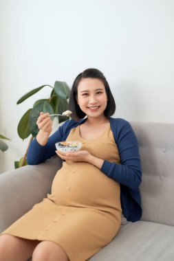 Kanepede sütlü ve sağlıklı kahvaltılı genç Asyalı hamile kadın.