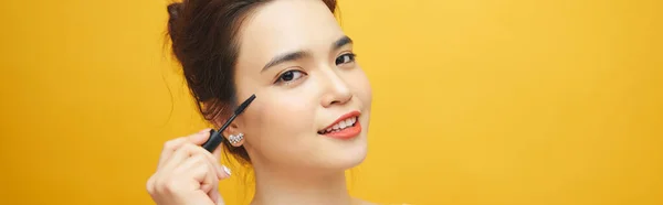 迷人的年轻女子在睫毛膏上涂上睫毛膏并在黄色背景上涂上化妆品的肖像 — 图库照片