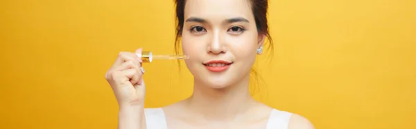 若い美しいアジアの女性は黄色の背景に皮膚のための血清のピペットを保持します — ストック写真
