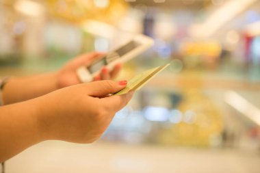 Alış veriş merkezinde cep telefonu ve kredi kartını tutan sahte el bulanık arkaplan.