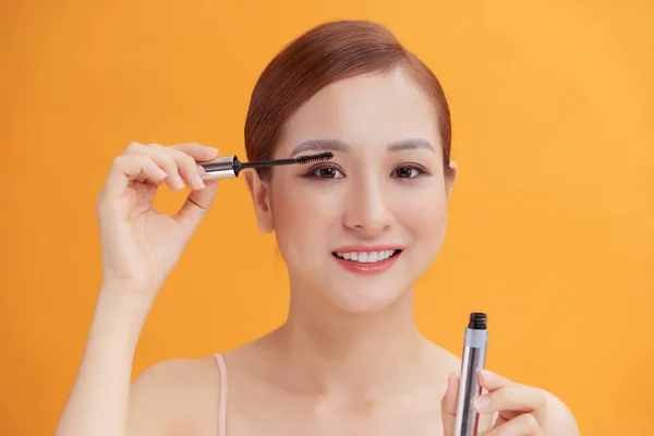 亚洲女性的特写镜头正在用黄色背景的睫毛膏 — 图库照片