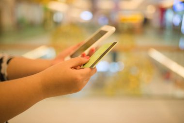 Alış veriş merkezinde cep telefonu ve kredi kartını tutan sahte el bulanık arkaplan.