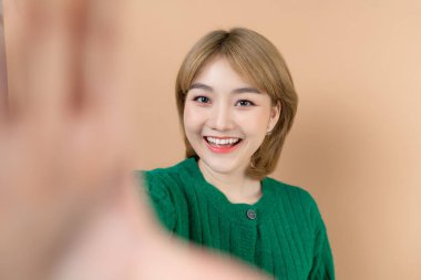 Makyajlı güzel Asyalı kız bej renkli bir stüdyoda özçekim yapıyor.