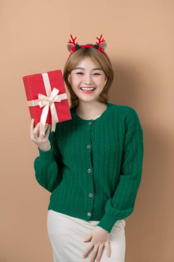 Kırmızı geyik boynuzları olan neşeli, komik genç kadın elinde bir Noel hediyesi tutuyor ve bej arka planda gülüyor.