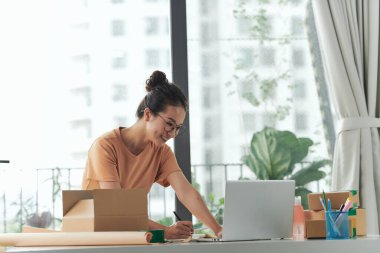 Kadın işyeri sahibi müşterilere paket hazırlarken gülümsüyor ve mutlu hissediyor.