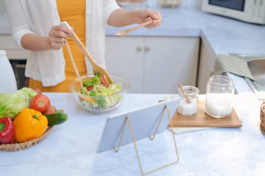 Mutfakta sebze hazırlayan ve tablet kullanan bir kadın.