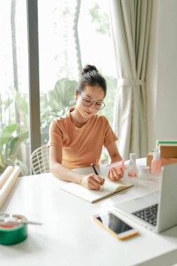 Genç ve çekici bir kız kozmetik ürünlerinin kalitesini kontrol ediyor, müşterileri uzaktan satın almak ve satın almak için satmaya hazırlanıyor.